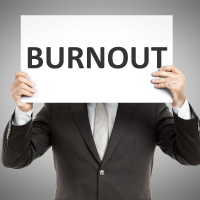 Homme en veston dont la tête est cachée derrière une affiche où il est inscrit le mot burnout.