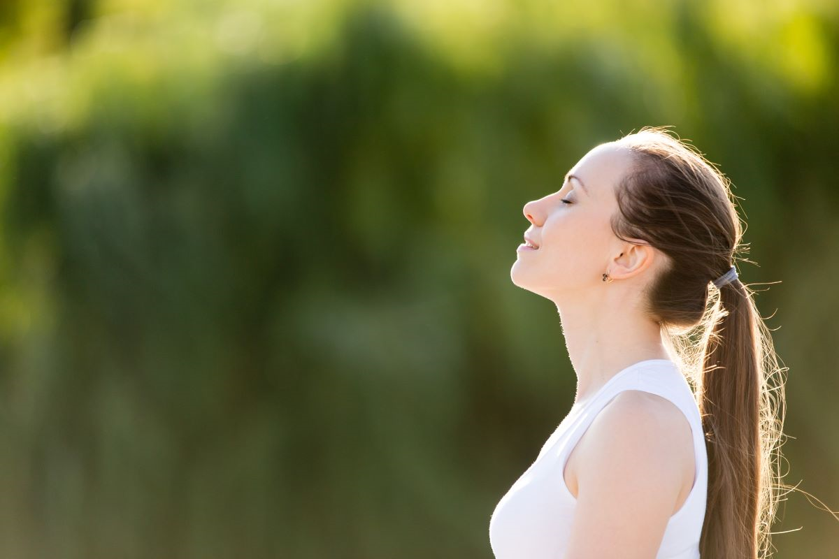 Jeune femme prenant une grande inspiration en plein air avec un air détendu représentant le bénéfice d'un accompagnement pour le stress et l'anxiété